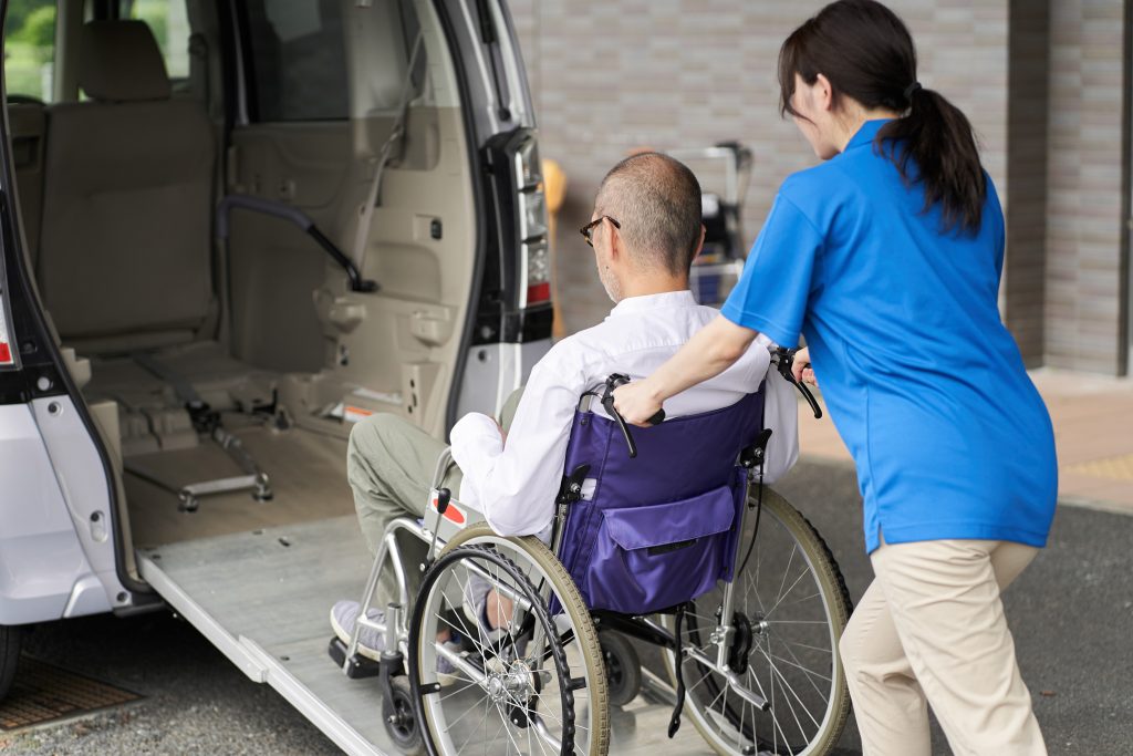 caregiver pusing old mans wheelchair into a taxi
